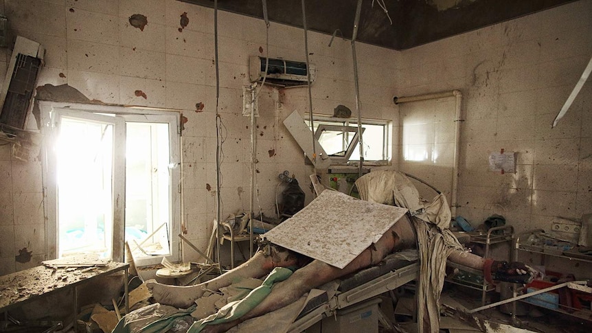 A dead body on a hospital operating table, buried under rubble.