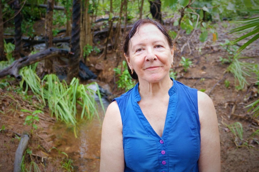 Smiling woman in blue blouse standing in a creek on a rainy day.