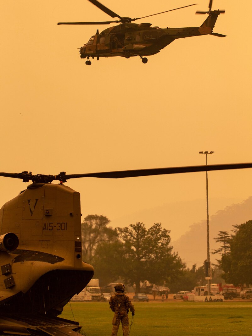 An Australian Army soldier watches a Blackhawk helicopter leave Omeo showgrounds surrounded by a yellow sky.