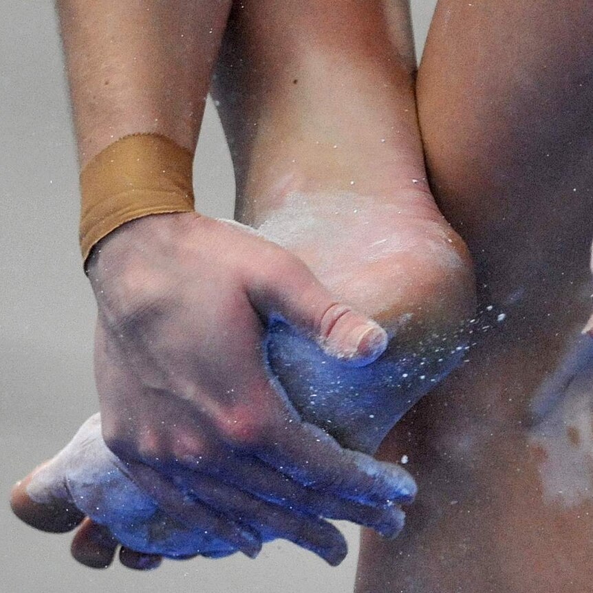 A female gymnast puts chalk on her feet.