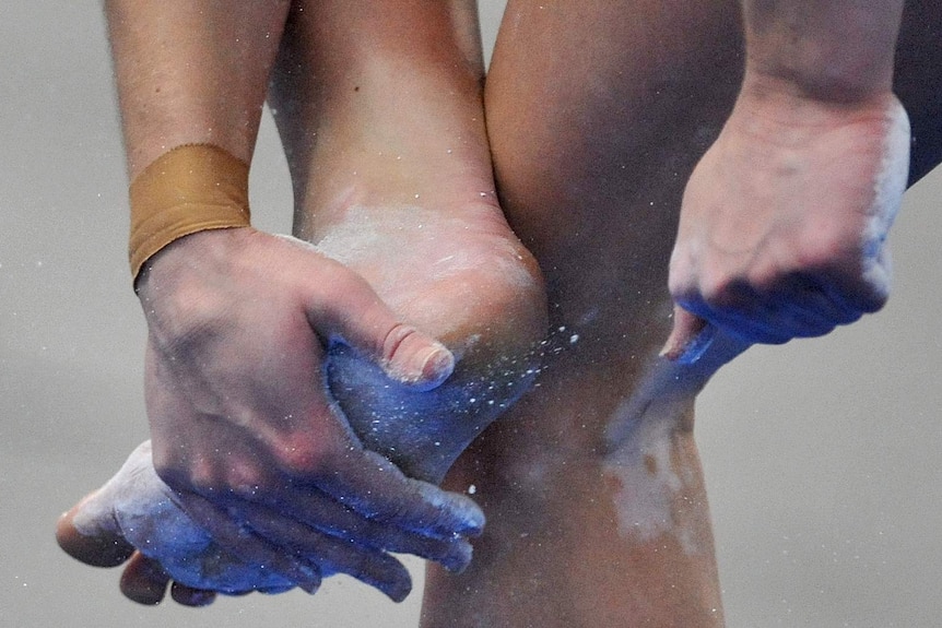 A female gymnast puts chalk on her feet.