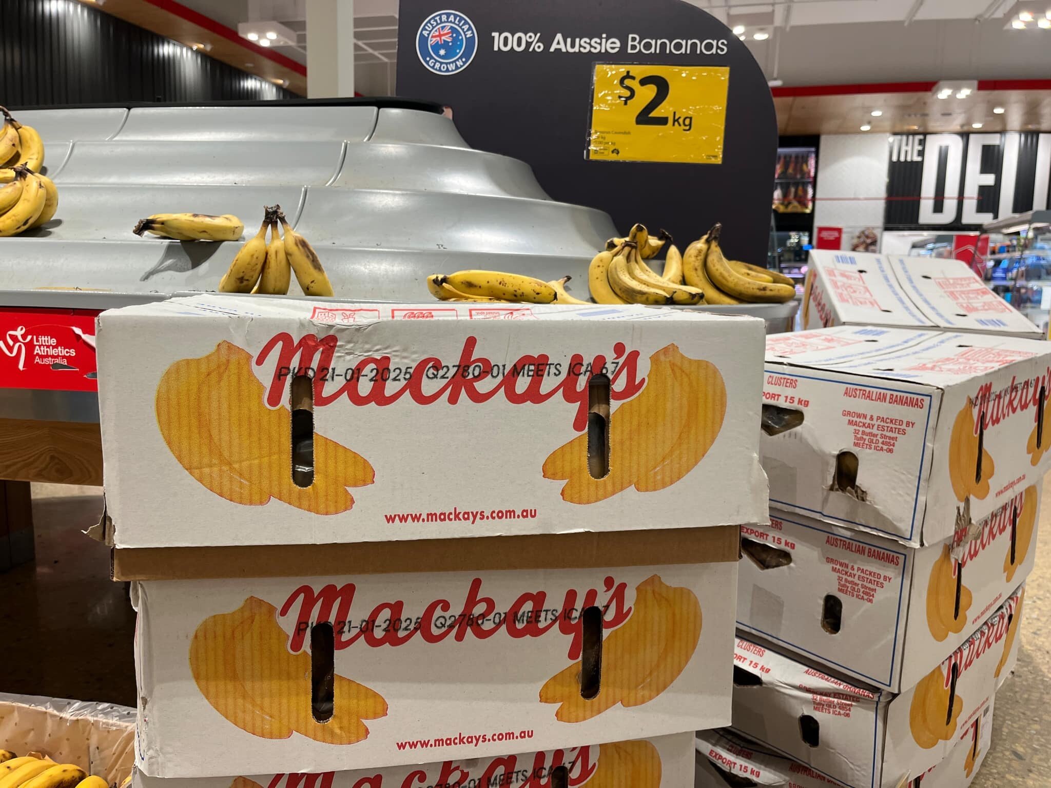 Banana boxes in front of a shelf with a few bananas on it in a supermarket.