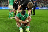 Jordie Barrett leans over to help Bundee Aki, who is sitting on the ground with his jersey over his face