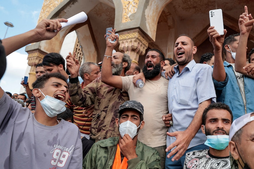 A group of men yelling with some wearing surgical masks and some not.