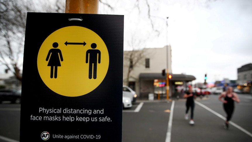 People jog past a sign urging social distancing