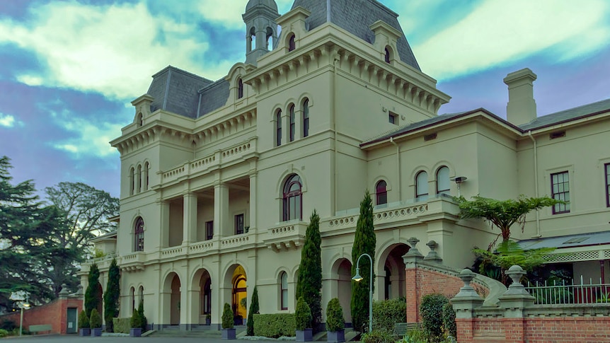 The front of a grand 1800s three-storey building, featuring arched entranceways and a bell tower.