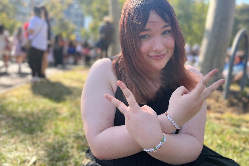 Trans woman with Taylor Swift bracelets doing the peace symbol with her hands.