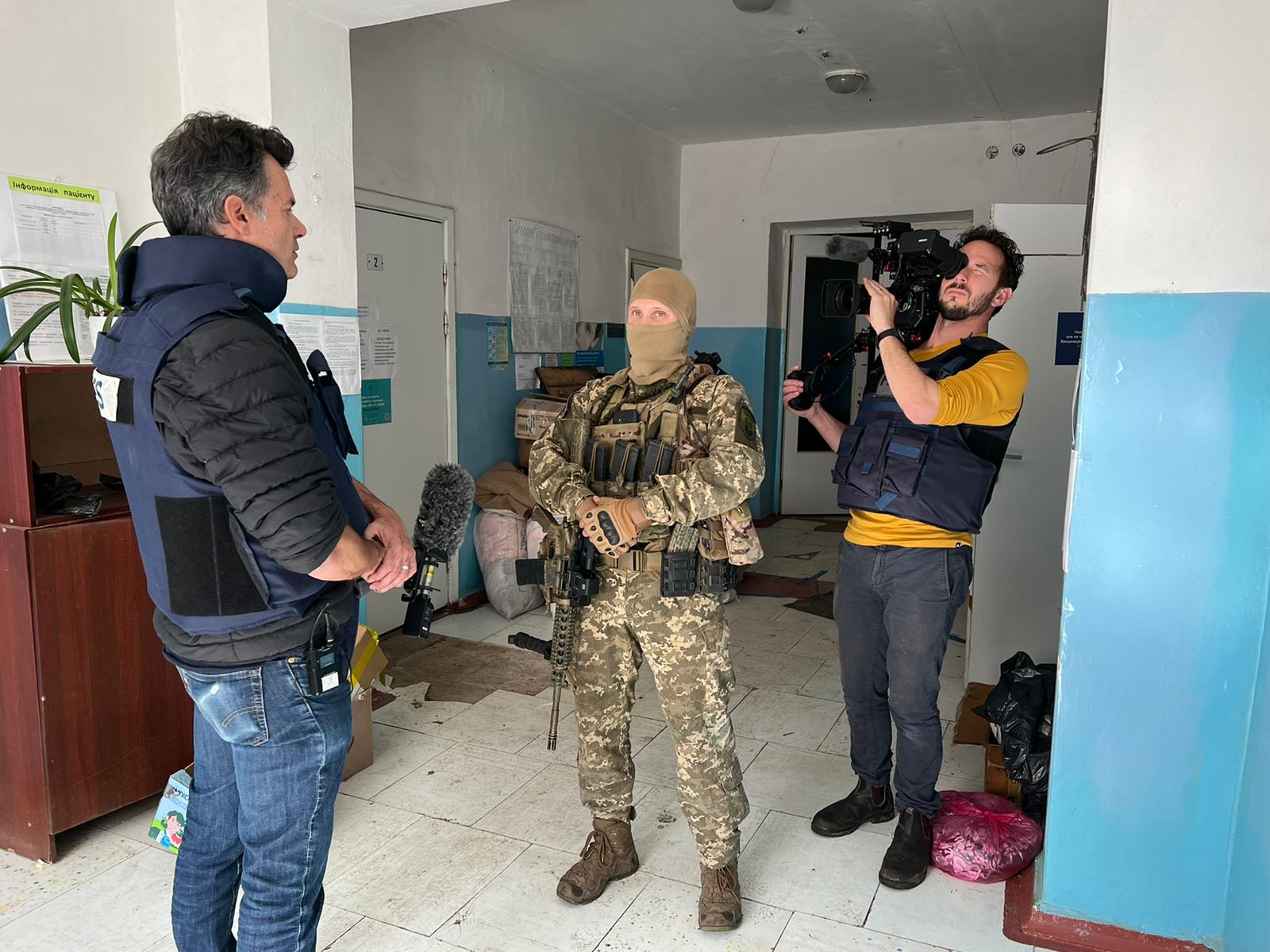 Cameraman filming man in bullet proof vest and soldier in uniform and balaclava.