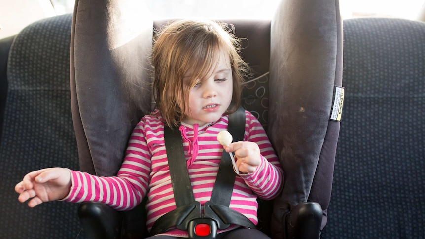 Jayde eats a lollypop in her childseat in the car