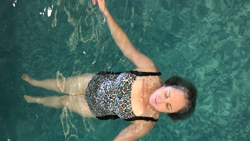 A woman floats in a pool wearing a one-piece swimsuit