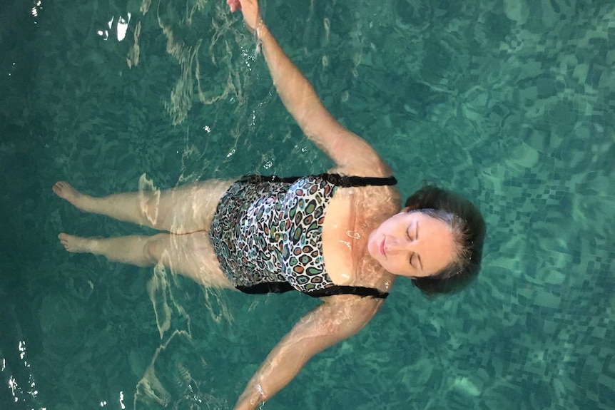 A woman floats in a pool wearing a one-piece swimsuit