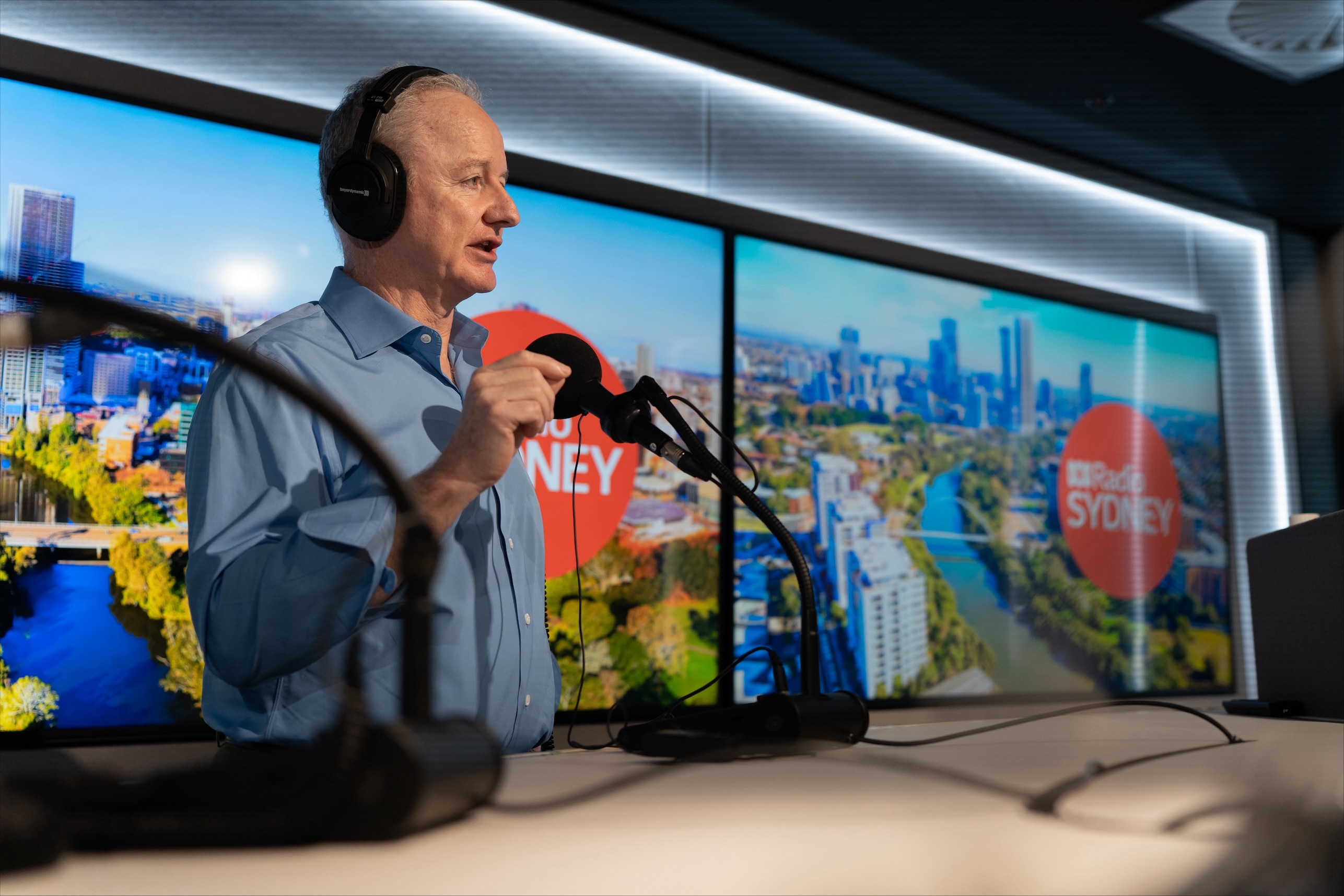 Hugh Marks gestures while speaking into a microphone in a radio studio.