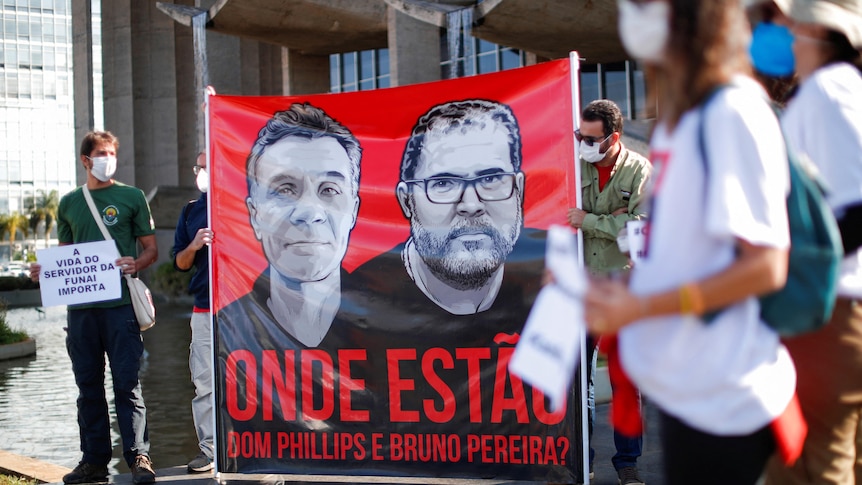 Protesters hold up large sign featuring images of two missing men in Brazil.