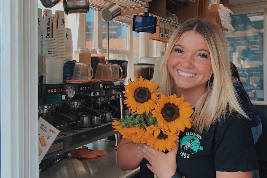 A young blonde woman holding sunflowers and smiling. 