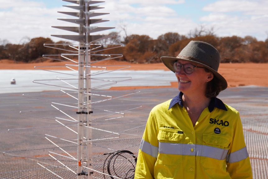 A woman named Sarah Pearce stands smiling next to a metal structure. 
