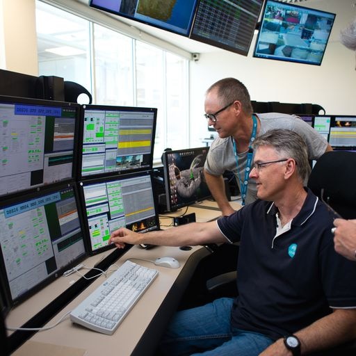 Two men in front of four computer monitors.