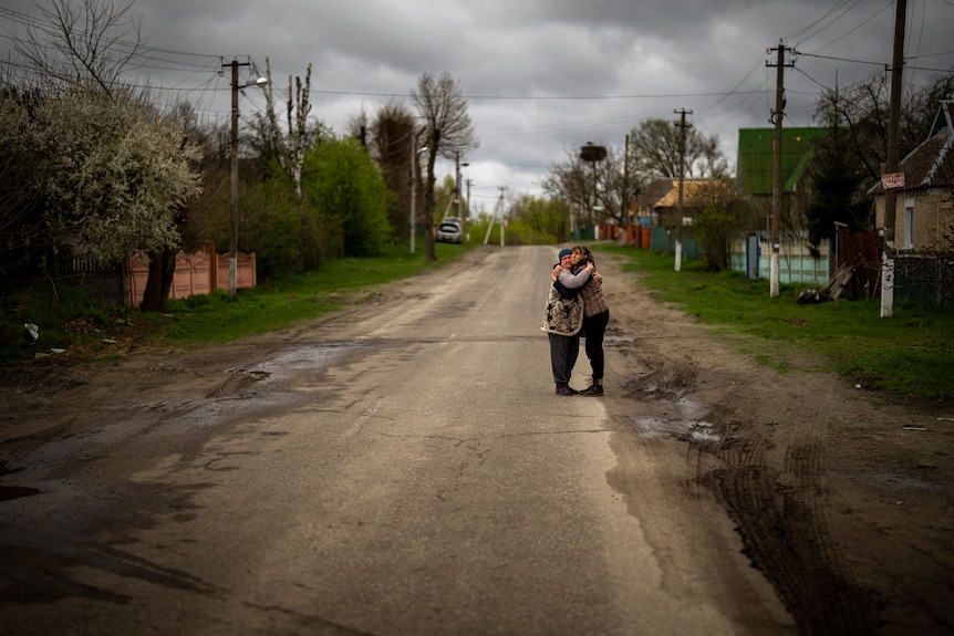 Two women hug on a suburban dirt road.