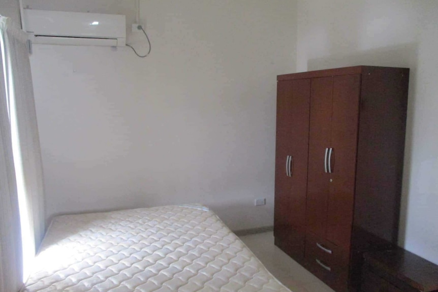 A small bedroom with a mattress, air conditioner and brown wardrobe.