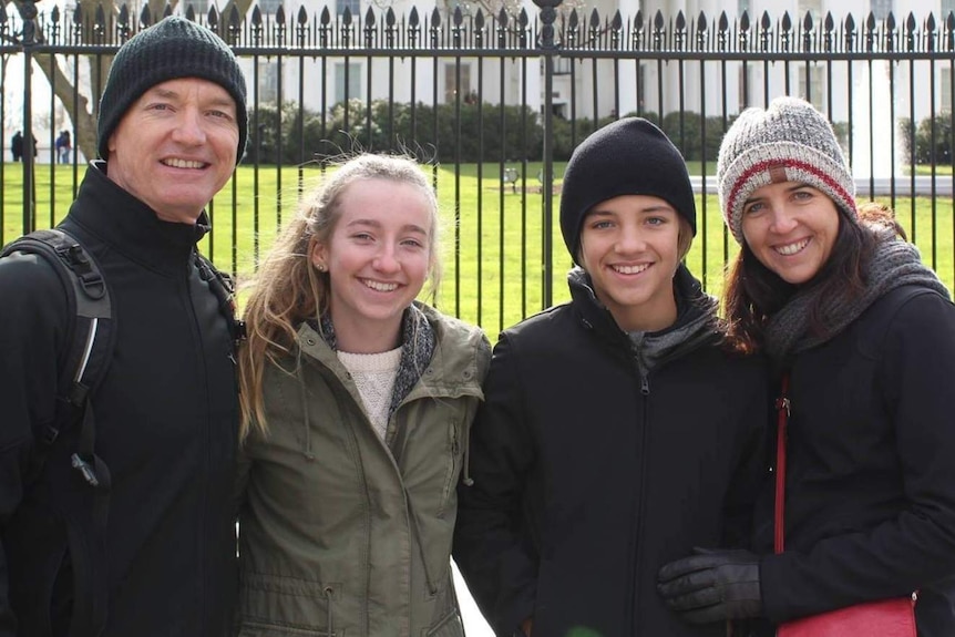 A mother and father stand with their two teenage children standing between them, all wearing beanies and jackets.
