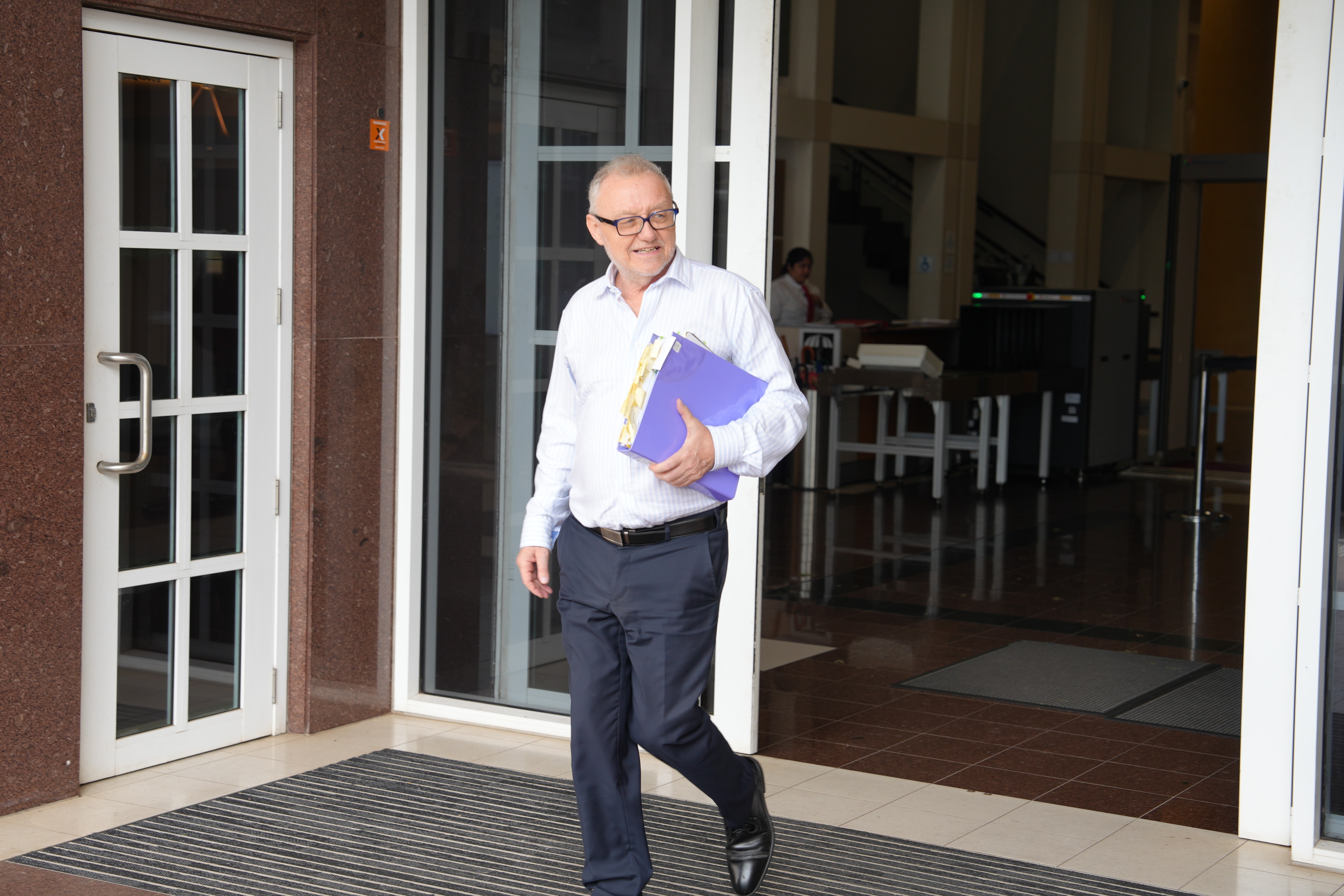 Um homem vestindo uma camisa branca carregando documentos ao sair do tribunal.