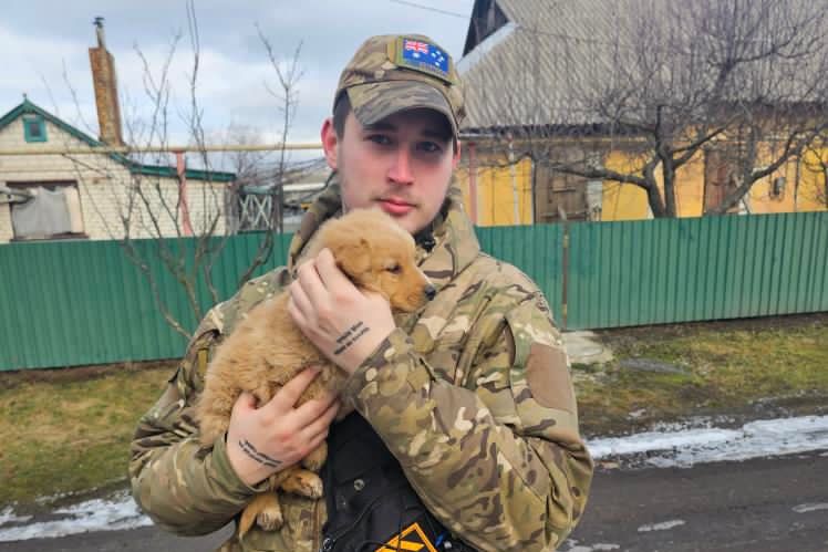 A young man wearing camouflaged clothing and holding a puppy.