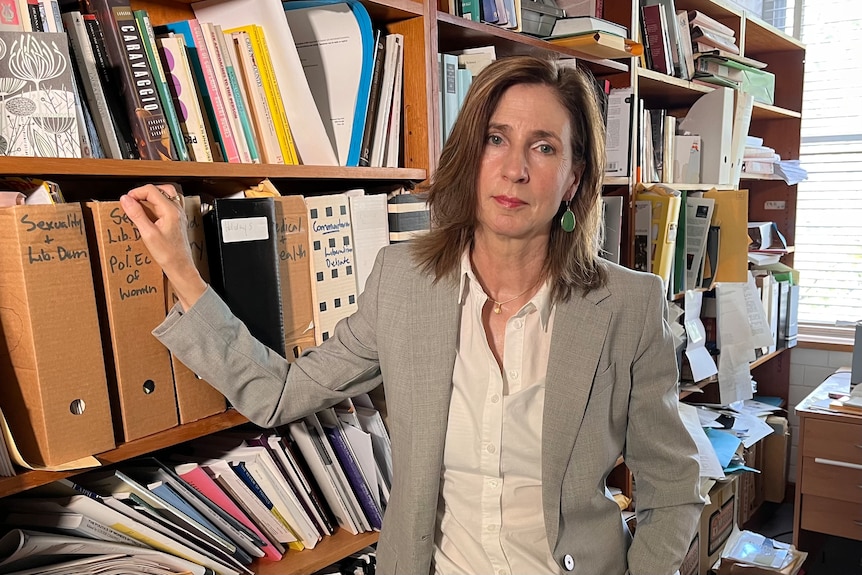 A woman stands in an office leaning against a bookcase filled with thick folders