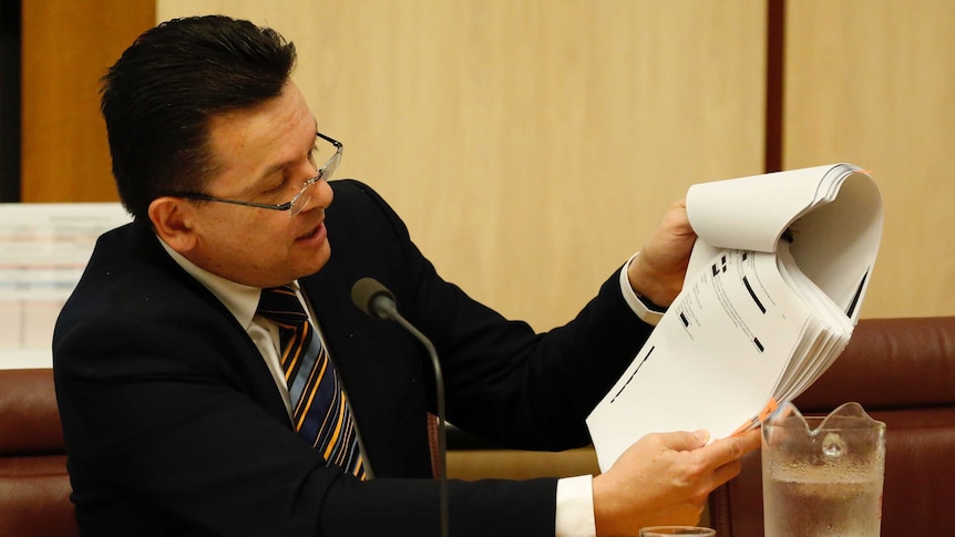 Senator Nick Xenophon talks into a microphone while looking at papers in the Senate Estimates.