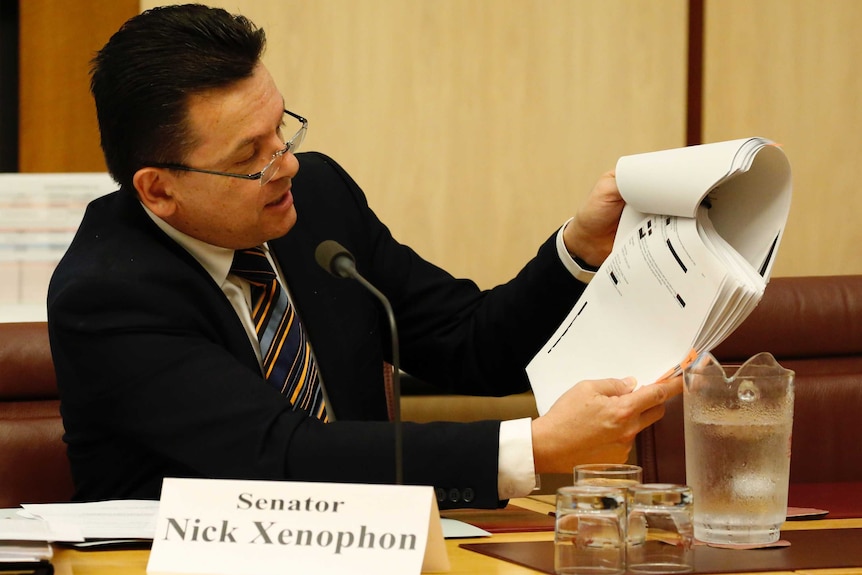 Senator Nick Xenophon talks into a microphone while looking at papers in the Senate Estimates.