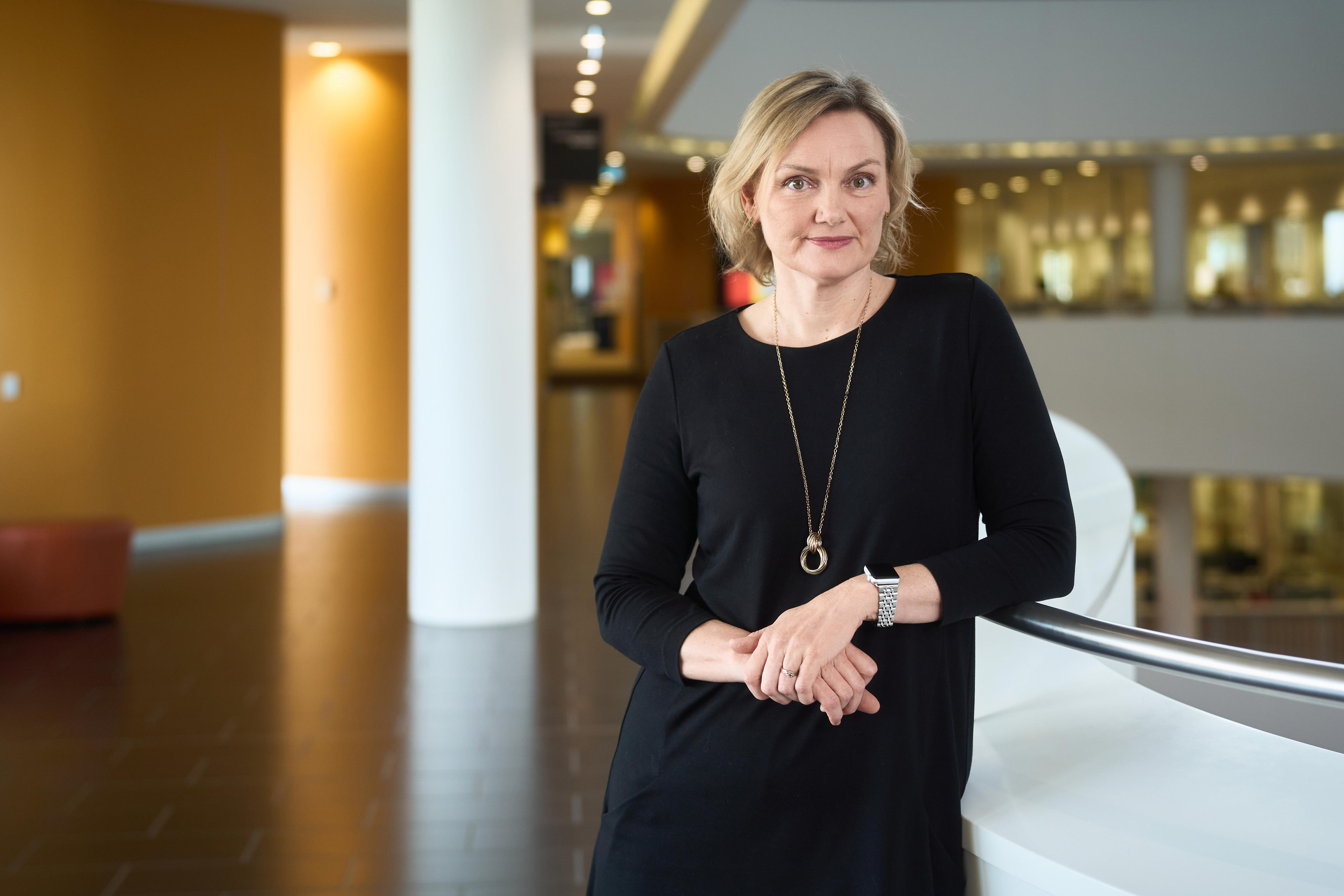 Primer plano medio de una mujer rubia con un suéter negro sonriendo a la cámara