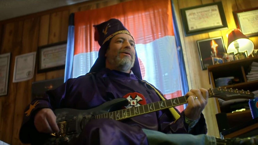 A man wearing purple robes and a purple hat, playing a guitar.