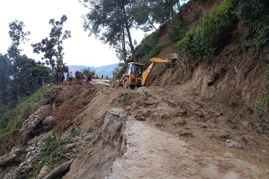 An earthmover works on a road that has been covered over and partially washed away in a landslide.