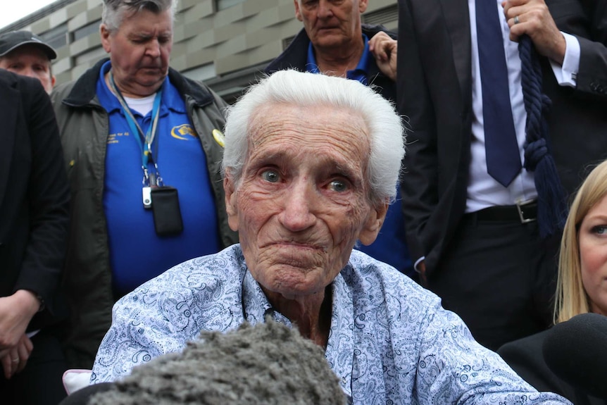 Elderly man close to tears surrounded by media with microphones outside a court in Perth