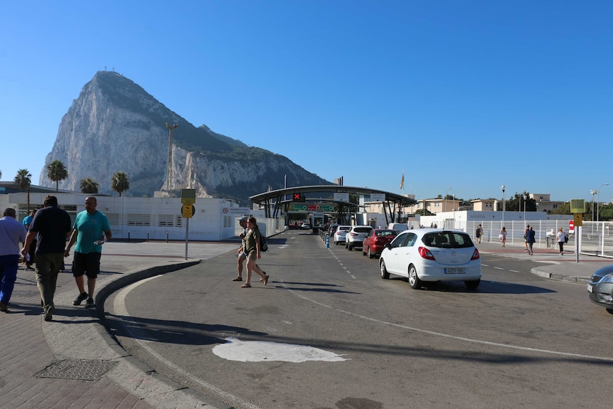 Cars line up at a toll booth, with the Rock of Gibraltar in the background.