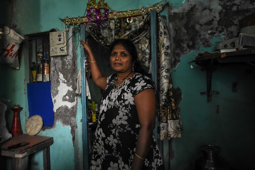 A woman standing inside her house leaning against her door frame.