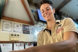 A smiling young woman with short, dark hair pulls a beer at a pub.