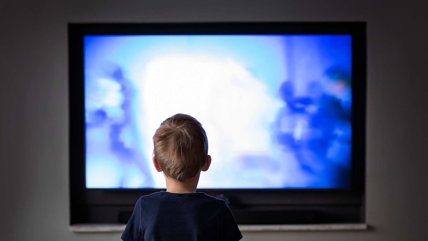 A small boy silhouetted by a television screen.