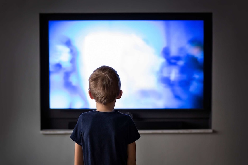A small boy silhouetted by a television screen.