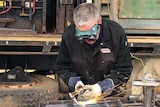 A man in goggle, wearing heavy gloves, works metal with an oxyacetylene torch.