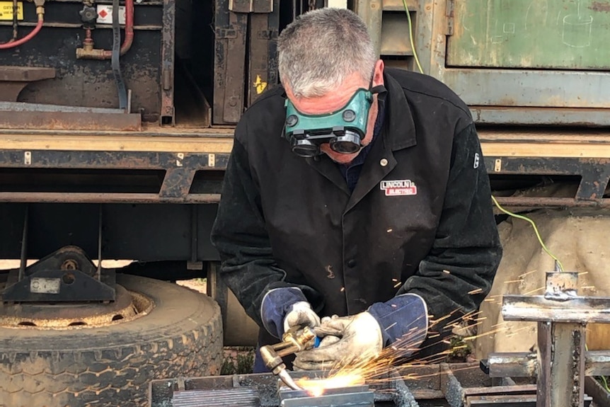 A man in goggle, wearing heavy gloves, works metal with an oxyacetylene torch.