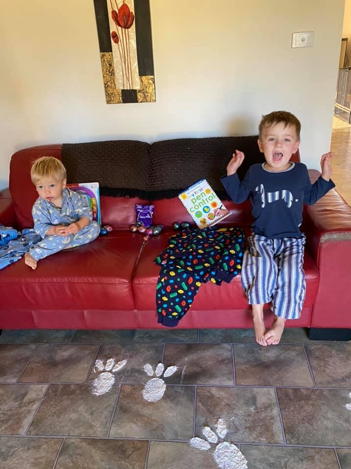 Two children sit on a sofa surrounded by Easter eggs.