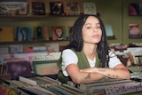Zoe Kravitz stands at a record shop front counter, surrounded by vinyl LPs