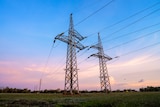 Two power transmission towers in the middle on an open field with a sunrise in the background., 