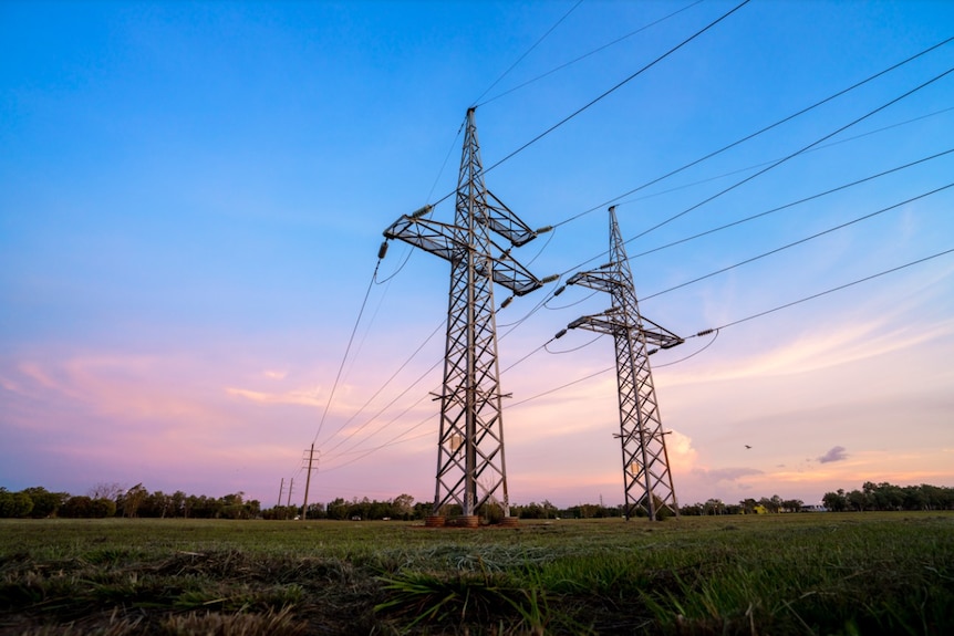 Two power transmission towers in the middle on an open field with a sunrise in the background. 
