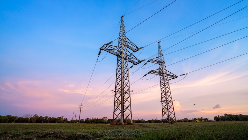 Two power transmission towers in the middle on an open field with a sunrise in the background.