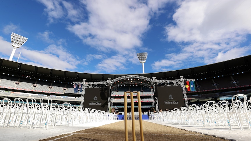A shot of the MCG, with cricket stumps surrounded by white chairs in front of a stage