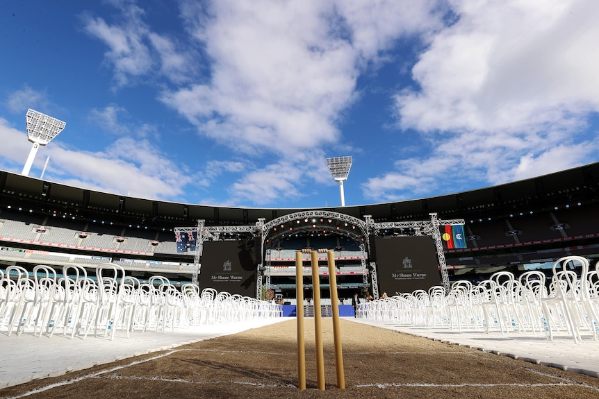 A shot of the MCG, with cricket stumps surrounded by white chairs in front of a stage