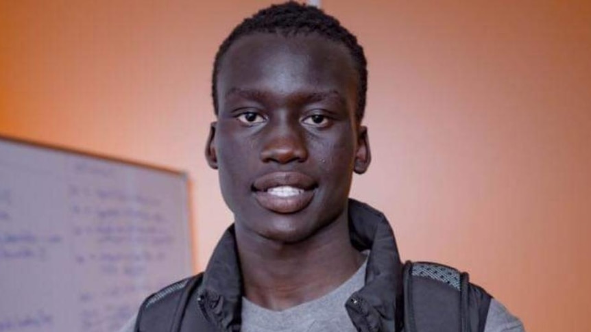 Aguer Lual Akec smiles as he holds out a pair of yellow Nike runners.