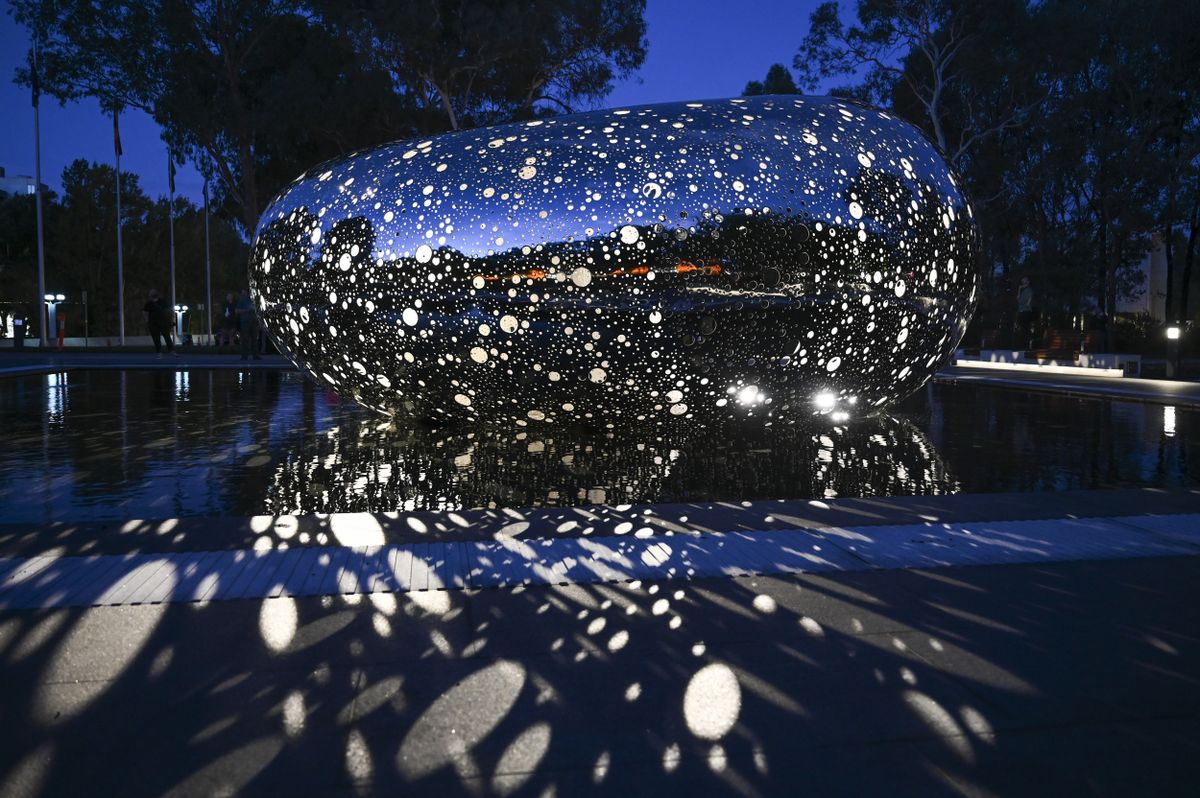 Light beams from a twisting silver sculpture outside an art gallery at night.