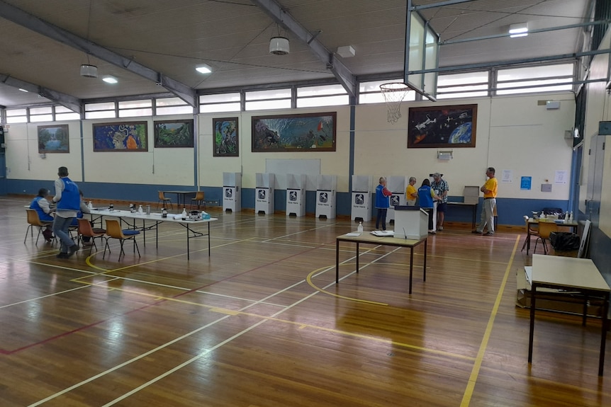 voters and scrutineers stand near polling booth in side a community sports hall