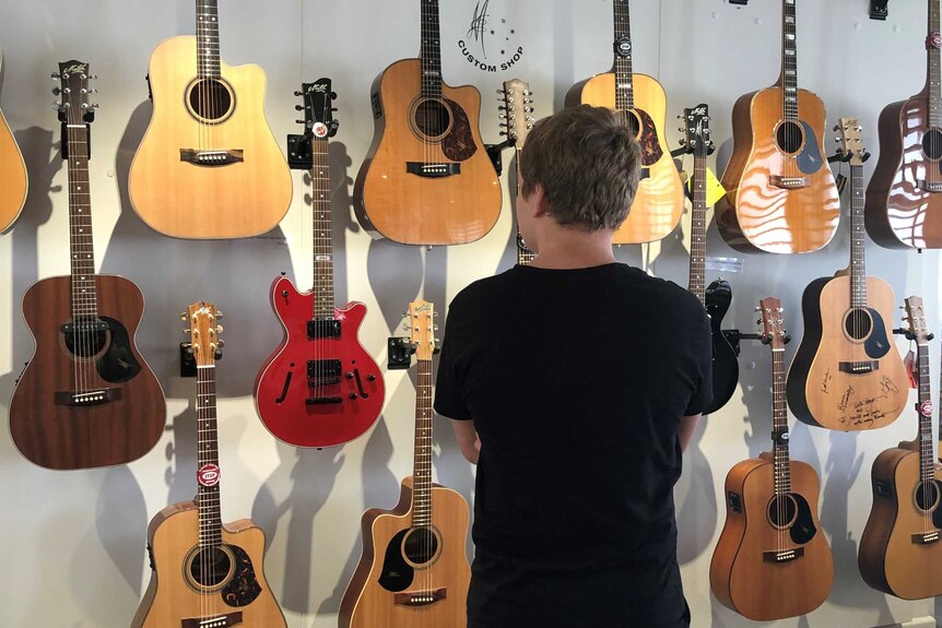 Corey Burke, with his back to the camera, looks at a wall of Maton guitars.